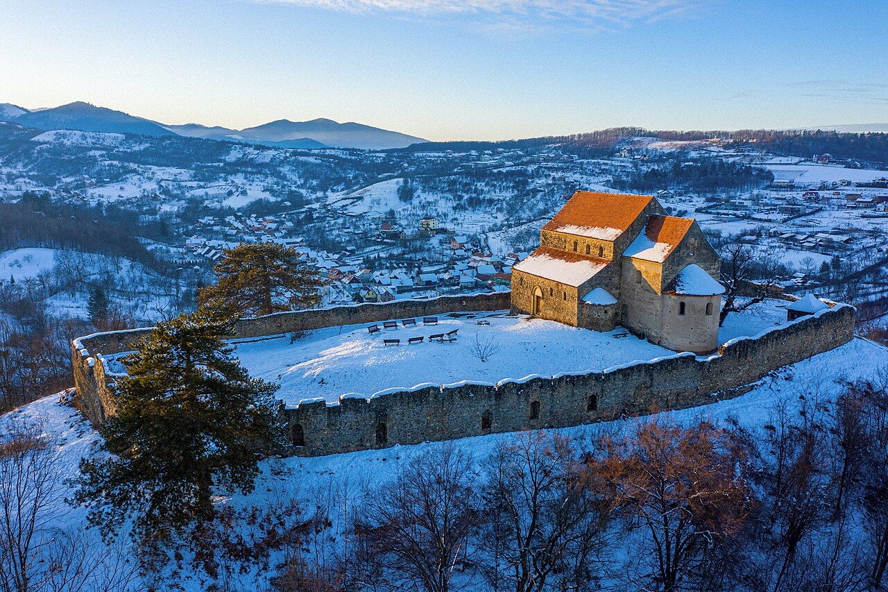 Fotografie aeriană oblică a bazilicii și incintei pe platoul înzăpezit.