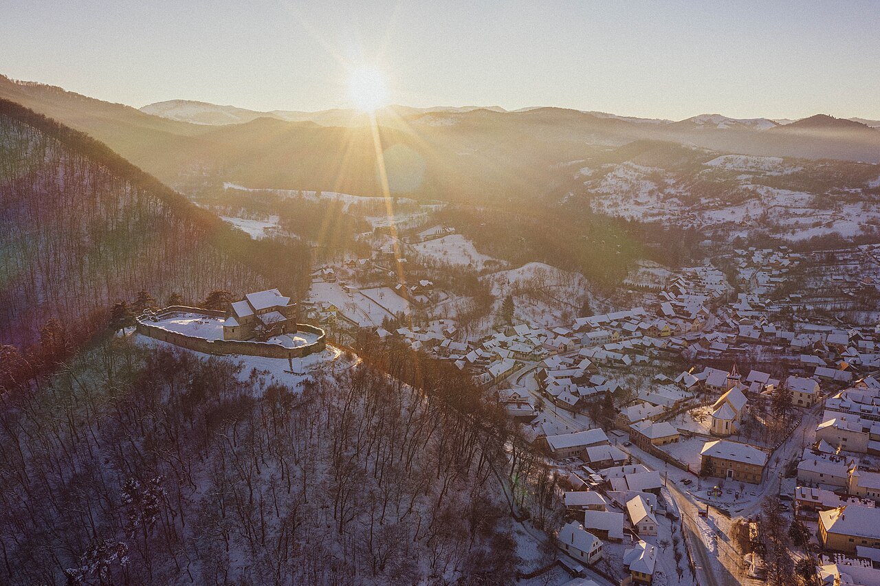 Fotografie aeriană largă a dealului fortificat și satului; detaliul bisericii este mic.
