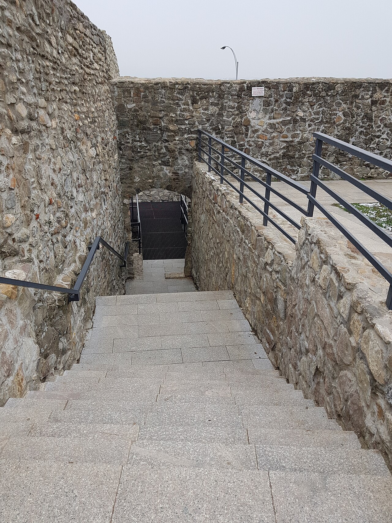 Scară coborând spre deschiderea din zid.
