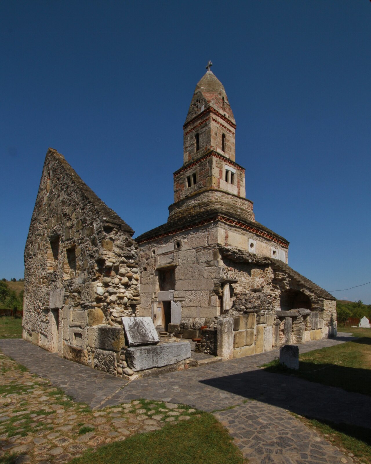 Biserica și anexele ruinate, vedere oblică însorită.