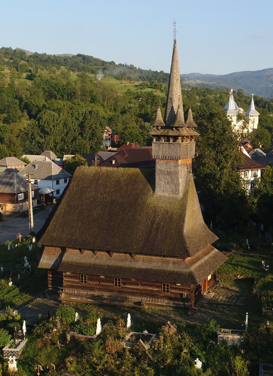 Vedere aeriană oblică a bisericii și cimitirului: acoperiș, turn și context.