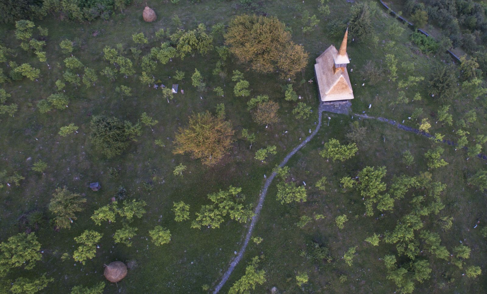 Vedere aeriană mai largă: biserica istorică și vegetația dealului Jbâr.